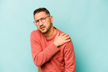 Mavi arka planda izole edilmiş genç İspanyol bir adam omuz ağrısı çekiyor..