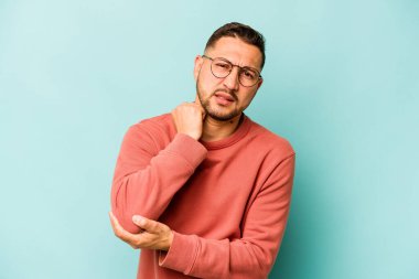 Genç İspanyol adam mavi arka planda izole edilmiş dirsek masajı yapıyor, kötü bir hareketin ardından acı çekiyor..