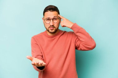 Genç İspanyol bir adam mavi arka planda izole edilmiş ve elinde bir ürün tutuyor..