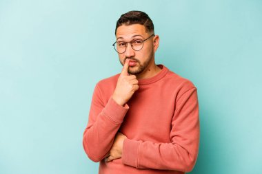 Genç İspanyol adam mavi arka planda izole edilmiş düşünüyor, bakıyor, yansıtıyor, düşünüyor, hayal kuruyor..