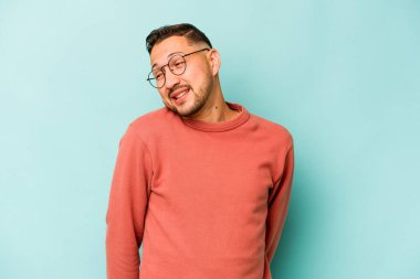 Mavi arka planda izole olmuş genç İspanyol adam gülüyor ve gözlerini kapıyor, rahatlamış ve mutlu hissediyor..