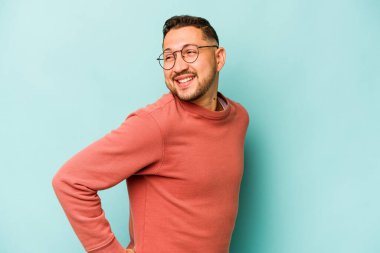 Mavi arka planda soyutlanmış genç bir İspanyol gülümsüyor, neşeli ve keyifli görünüyor..