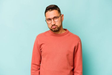 Genç İspanyol adam mavi arka planda izole edilmiş üzgün, ciddi yüz, mutsuz ve hoşnutsuz hissediyor.