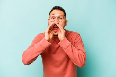 Genç İspanyol bir adam mavi arka planda izole edilmiş. Dedikodu yapıyor, bir şeyleri bildiriyor..