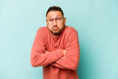 Mavi arka planda izole edilmiş genç bir İspanyol omuz silker ve gözleri açık kalır..