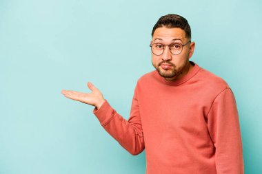 Mavi arka planda izole edilmiş genç İspanyol bir adam avucunun içinde bir fotokopi alanı ve belinde bir el daha gösteriyor..