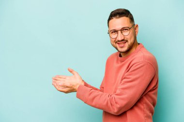 Mavi arka planda izole edilmiş genç İspanyol bir adam avucunun içinde bir kopyasını tutuyor..