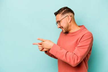Genç İspanyol adam mavi arka planda izole edilmiş başparmak uzakta, gülüyor ve kaygısız.