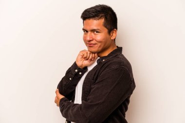 Beyaz arka planda izole olmuş genç İspanyol adam gülümsüyor ve kendinden emin, elleriyle çeneye dokunuyor..