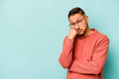 Mavi arka planda izole edilmiş, üzgün ve dalgın hisseden genç bir İspanyol fotokopi odasına bakıyor..