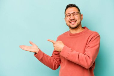 Mavi arka planda izole edilmiş genç İspanyol bir adam heyecanlı bir şekilde avuç içinde bir kopyasını tutuyor..