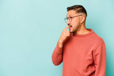 Mavi arka planda izole olmuş genç İspanyol bir adam rahatlamış bir şeyin fotokopi odasına baktığını düşünüyor..