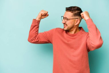 Mavi arka planda izole edilmiş genç İspanyol bir adam zaferden sonra yumruk kaldırıyor, kazanan konsept..