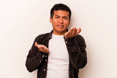 Beyaz arka planda izole edilmiş genç İspanyol adam kollarıyla ölçeği yapıyor, mutlu ve kendinden emin hissediyor..