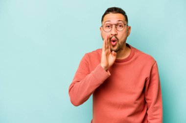 Mavi arka planda izole edilmiş genç İspanyol bir adam gizli bir sıcak fren haberi veriyor ve yana bakıyor.