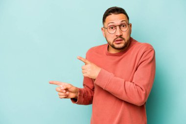 Mavi arka planda izole edilmiş genç İspanyol adam işaret parmağıyla fotokopi alanını işaret ederek şok oldu..