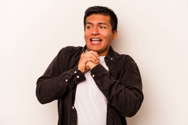 Beyaz arka planda izole edilmiş genç İspanyol adam ellerini çenesinin altında tutuyor ve mutlu bir şekilde yan tarafa bakıyor..