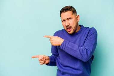 Mavi arka planda izole edilmiş genç İspanyol adam işaret parmaklarıyla fotokopi alanını işaret ederek heyecan ve arzuyu ifade ediyor..