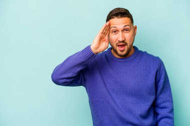 Mavi arka planda izole edilmiş genç bir İspanyol yüksek sesle bağırıyor, gözleri açık ve elleri gergin tutuyor..