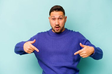 Genç İspanyol bir adam mavi arka planda izole edilmiş. Parmakları aşağıda, olumlu hisler içinde..