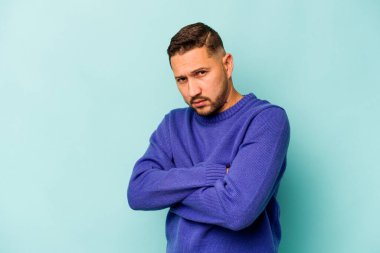 Mavi arka planda izole edilmiş, hoşnutsuzca kaşlarını çatmış, kollarını kavuşturmuş genç bir İspanyol..