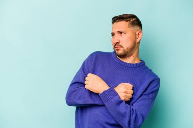 Mavi arka planda izole edilmiş genç bir İspanyol kafası karışmış, kuşkulu ve güvensiz hissediyor..