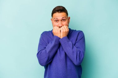 Mavi arka planda izole edilmiş, tırnak yiyen, gergin ve endişeli genç bir adam..