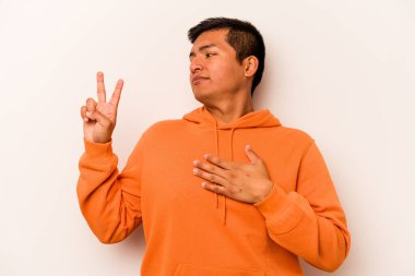 Genç İspanyol bir adam beyaz arka planda izole edilmiş yemin ediyor, elini göğsüne koyuyor..