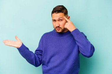 Mavi arka planda izole edilmiş genç İspanyol adam işaret parmağıyla bir hayal kırıklığı gösteriyor..