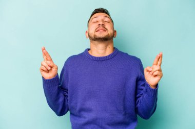 Genç İspanyol adam mavi arka planda izole edilmiş şans dilemek için şans diliyor.