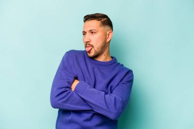 Genç İspanyol adam mavi arka planda izole edilmiş komik ve dost canlısı bir dil uzatıyor..