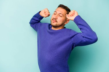 Mavi arka planda izole edilmiş genç İspanyol adam kollarını uzatıyor, rahat bir konumda..