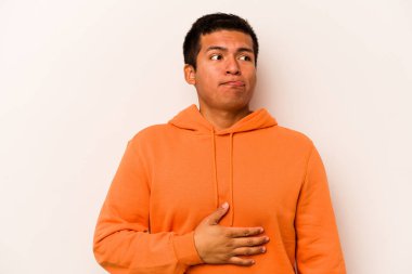 Beyaz arka planda izole edilmiş genç İspanyol adam karnına dokunuyor, nazikçe gülümsüyor, yemek yiyor ve tatmin oluyor..