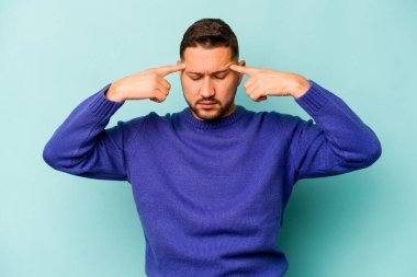 Mavi arka planda izole edilmiş genç İspanyol bir adam bir göreve odaklanmış, işaret parmaklarını işaret ediyor..