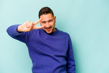 Genç İspanyol adam mavi arka planda izole edilmiş dans ediyor ve eğleniyor.