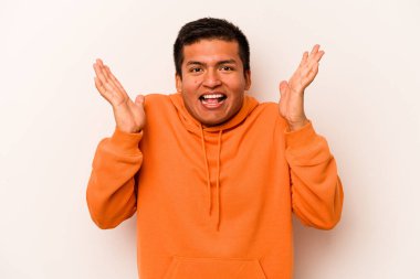 Latin kökenli genç bir adam beyaz arka planda izole edilmiş. Hoş bir sürprizle karşılaşıyor, heyecanlı ve el kaldırıyor..