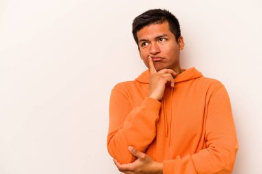 Beyaz arka planda izole edilmiş genç bir İspanyol şüpheli ve şüpheci bir ifadeyle yana bakıyor..