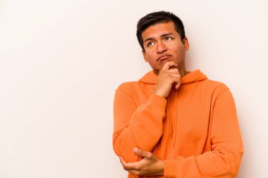 Beyaz arka planda izole edilmiş genç bir İspanyol şüpheli ve şüpheci bir ifadeyle yana bakıyor..