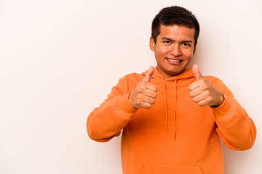 Beyaz arka planda izole edilmiş genç İspanyol adam gülümsüyor ve başparmağını kaldırıyor.