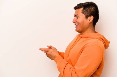 Latin kökenli genç adam beyaz arka planda izole edilmiş, başparmak uzakta, gülüyor ve kaygısız..