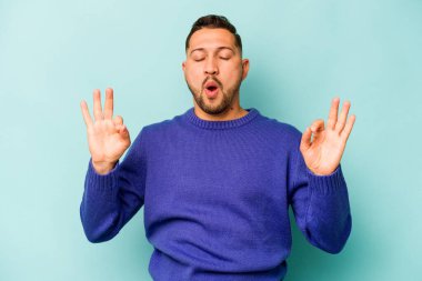 Mavi arka planda izole olmuş genç İspanyol adam sıkı çalışma gününden sonra rahatlıyor, yoga yapıyor..