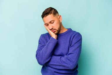 Mavi arka planda izole edilmiş genç bir İspanyol. Sıkılmış, yorgun ve dinlenmeye ihtiyacı var..