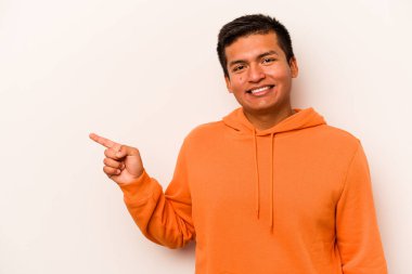 Beyaz arka planda izole edilmiş genç İspanyol adam işaret parmağıyla işaret ederek gülümsüyor..
