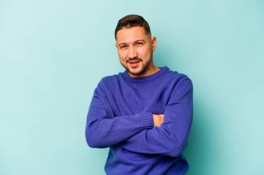 Mavi arka planda kendini güvende hisseden, kararlılıkla kollarını kavuşturan genç İspanyol bir adam..