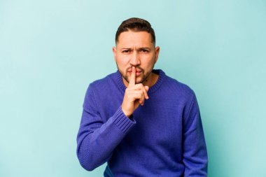 Mavi arka planda izole edilmiş genç İspanyol bir adam ya sır saklıyor ya da sessizlik istiyor..