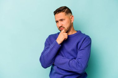 Mavi arka planda izole edilmiş genç İspanyol bir adam virüs ya da enfeksiyon yüzünden boğazında ağrı hissediyor..