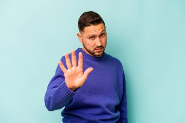 Genç İspanyol bir adam mavi arka planda izole edilmiş, tiksinti gösteren birini reddediyor..