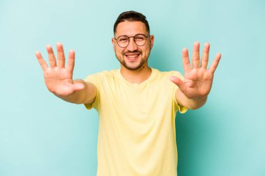 Mavi arka planda izole edilmiş genç İspanyol adam on numarayı elleriyle gösteriyor..