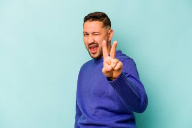 Mavi arka planda izole edilmiş genç İspanyol adam iki numarayı parmaklarıyla gösteriyor..