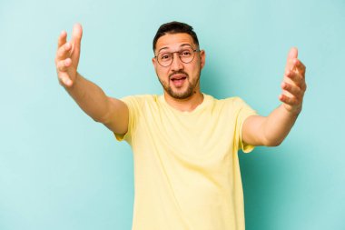 Latin kökenli genç bir adam mavi arka planda zaferi ya da başarıyı kutlarken şaşırmış ve şok olmuştu..